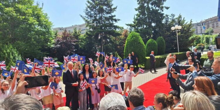 Blair pritet nga fëmijët në oborrin e Kuvendit me flamuj të Kosovës e Britanisë së Madhe